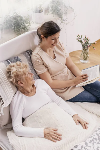 Hilfsbereite Helferin Liest Einer Älteren Frau Die Bett Liegt Ein — Stockfoto