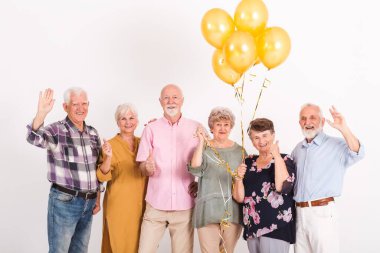 Beyaz iç mekan, bir grup kıdemli mutlu arkadaş ellerinde balonlarla.