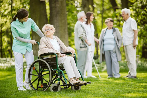 在疗养院花园有照顾者的老年病人群体 — 图库照片