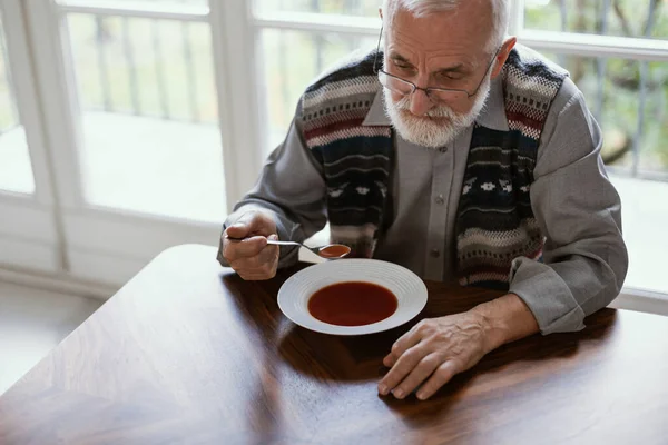Older sad man eating dinner alone in the apartment