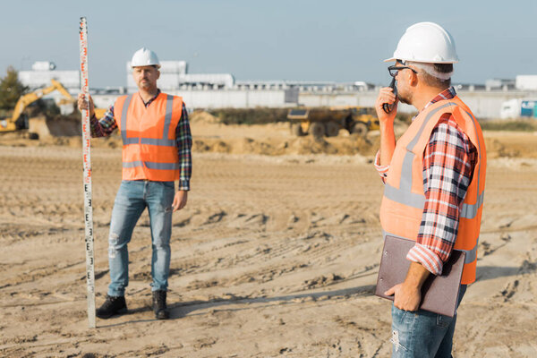 Two builders in orange vests and helmets working on the road construction field