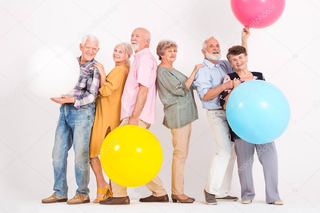 Six senior friends with big colorful balloons smiles in empty white interior