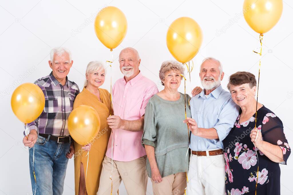 Group of senior people with yellow balloons standing in empty white room