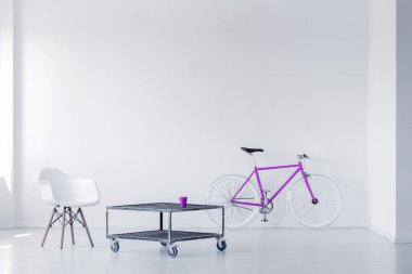 Mor bisiklet, sandalye ve metal sehpa minimalist bir odanın içinde. Gerçek fotoğraf.
