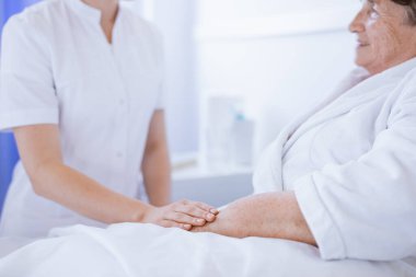 Genç hemşirenin yaşlı kadının elini tuttuğu yakın plan.