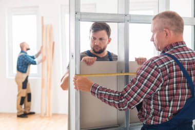 İki inşaatçı alçıpanı metal çerçeveye koyuyor.