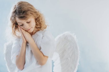 Kanatlı, beyaz cüppeli, sarı saçlı kızın resmi.