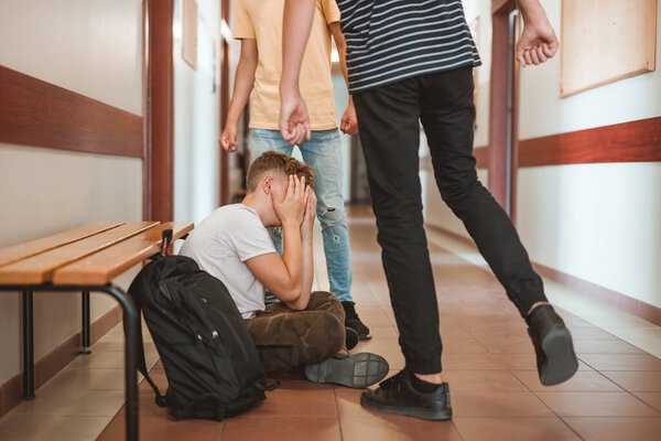 Rude teenage kids bulling their poor classmate on the school corridor