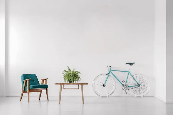 Bike, armchair and table in a white room interior. Empty wall, place your poster. Real photo