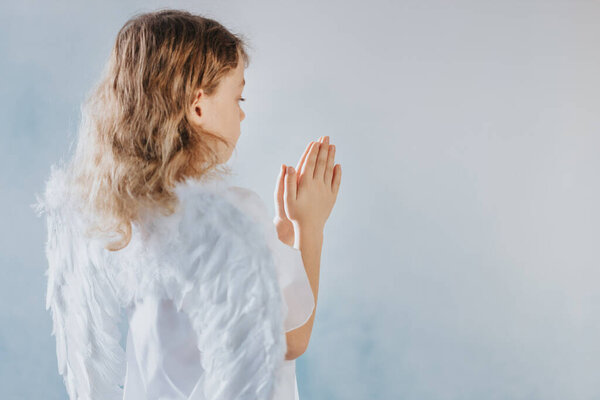 Little angel in white robe and blond hair praying