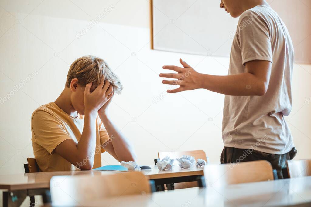 Mean boys bullying a classmate sitting at school desk