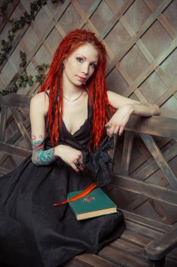 Dövmeli kız kırmızı dreadlocks bir kitap ve bir bankta oturan kalem tutan bir şey hayal