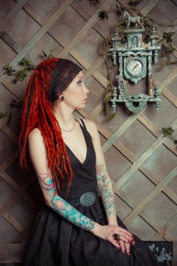 Dövmeli kız kırmızı dreadlocks saat duvara bakarak