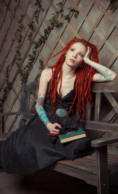 Dövmeli kız kırmızı dreadlocks bir kitap ve bir bankta oturan kalem tutan bir şey hayal