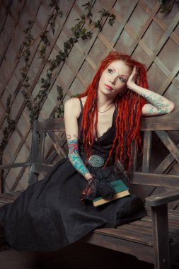 Dövmeli kız kırmızı dreadlocks bir kitap ve bir bankta oturan kalem tutan bir şey hayal