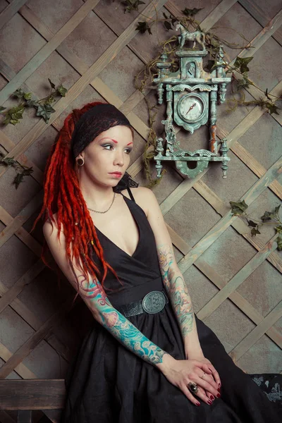 Tattooed girl with red dreadlocks,  looking at the clock on the wall — Stock Photo, Image