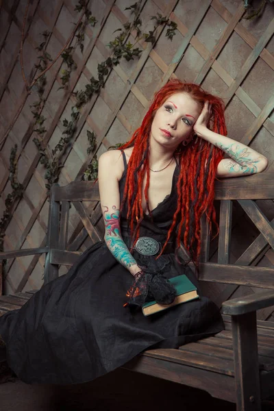 Dövmeli kız kırmızı dreadlocks bir kitap ve bir bankta oturan kalem tutan bir şey hayal