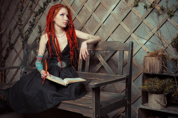 Dövmeli kız kırmızı dreadlocks bir kitap ve bir bankta oturan kalem tutan bir şey hayal