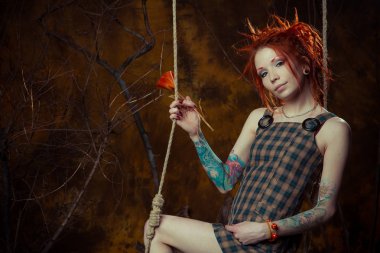 Genç, masum bir dövmeli kız salıncak üzerinde turuncu dreadlocks ile