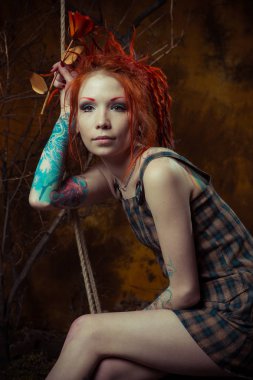 Genç, masum bir dövmeli kız salıncak üzerinde turuncu dreadlocks ile