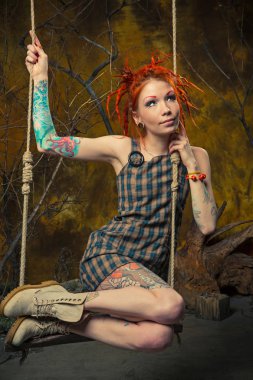 Genç, masum bir dövmeli kız salıncak üzerinde turuncu dreadlocks ile