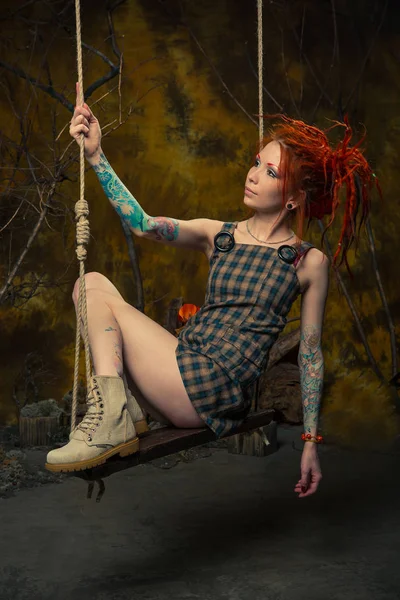 Genç, masum bir dövmeli kız salıncak üzerinde turuncu dreadlocks ile