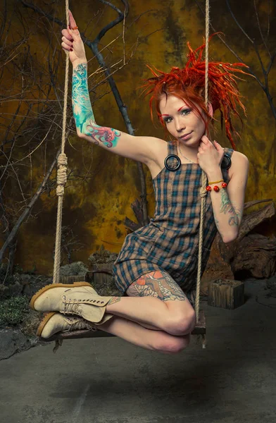 Genç, masum bir dövmeli kız salıncak üzerinde turuncu dreadlocks ile