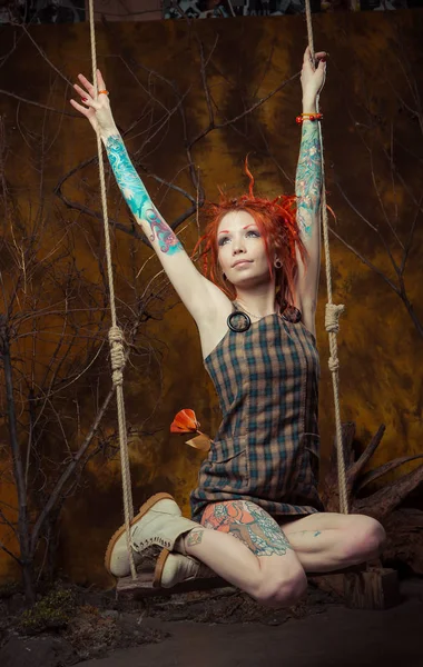 Genç, masum bir dövmeli kız salıncak üzerinde turuncu dreadlocks ile