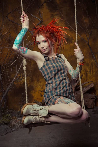 Молода, невинна татуйована дівчина з помаранчевими дредлоками на гойдалках — стокове фото
