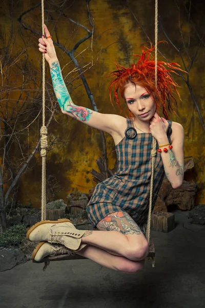 Молода, невинна татуйована дівчина з помаранчевими дредлоками на гойдалках — стокове фото