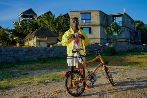 Dezembro de 2019. África, Uganda, uma aldeia perto de Entebbe. Um homem elegante e bem vestido com roupas brilhantes e óculos brancos, em uma bicicleta — Fotografia de Stock