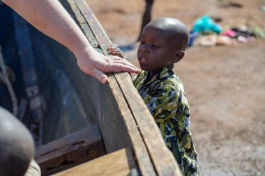Aralık, 2019. Afrika, Uganda, Victoria Gölü, koyu tenli küçük bir çocuk kayığa binen şişman bir turistin beyaz eline bakıyor..