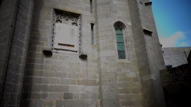 Julay, 2019, Francia, Mont Saint-Michel es una ciudad isla-fortaleza en la costa. Movimiento de la cámara en las paredes de mampostería de la abadía gótica hacia arriba, cielo azul — Vídeo de stock