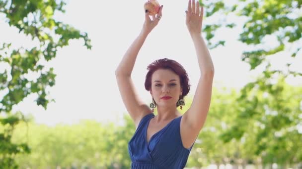 Елегантна руда жінка в блакитній сукні танцює з яблуком в руках — стокове відео