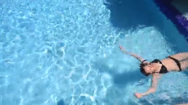 Красива дівчина в чорному купальнику плаває у воді — стокове відео