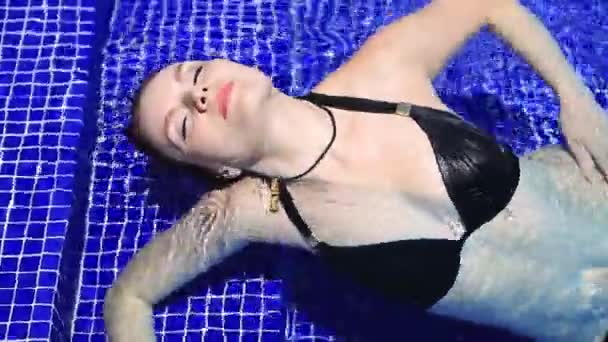 Menina bonita em um maiô preto na água nos degraus da piscina — Vídeo de Stock