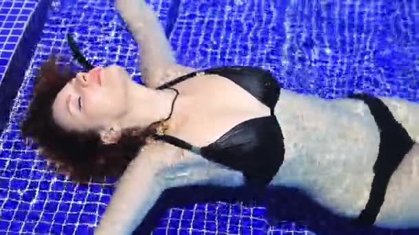 Красивая девушка в черном купальнике в воде на ступенях бассейна — стоковое видео