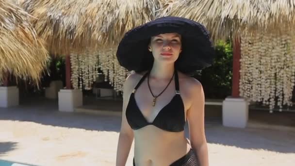 Ein Mädchen mit schwarzem Hut und Badeanzug entspannt am Pool — Stockvideo