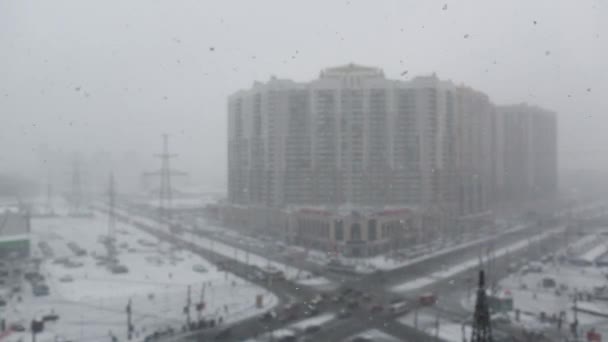 Snöstorm, snö faller i flingor och suddar ut utsikten över stadskärnan och en flervåningshus i utkanten av en stor stad — Stockvideo