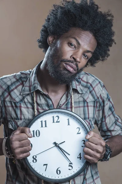 Afroamerikaner em uma camisa quadriculada segura o grande relógio branco — Fotografia de Stock