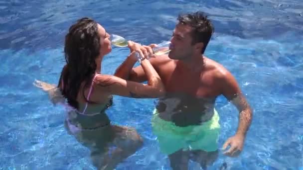 Хлопець і дівчина п'ють шампанське в басейні і сміються — стокове відео