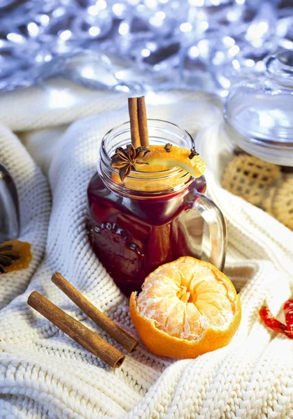 Mulled wine in a jar with orange, cinnamon sticks, anise and mandarine on a knitted sweater