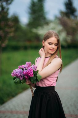 Sevimli kız pembe bluz ve siyah etek güzel çiçekli ağaçlar arka plan üzerinde fotoğrafçılar için poz veriyor. Bahar. Sakura.