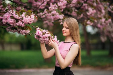 Sevimli kız pembe bluz ve siyah etek güzel çiçekli ağaçlar arka plan üzerinde fotoğrafçılar için poz veriyor. Bahar. Sakura.
