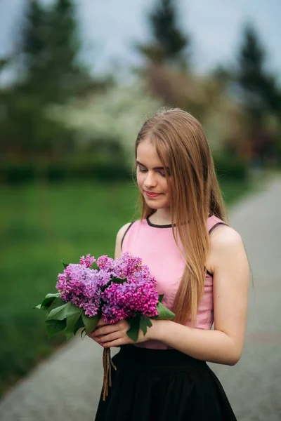 Charming girl in pink blouse and black skirt poses for photographers on the background of beautiful flowering trees. Spring. Sakura. — Stock Photo, Image