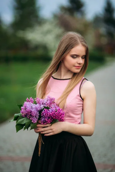 Encantadora chica en blusa rosa y falda negra posa para fotógrafos en el fondo de hermosos árboles con flores. Primavera. Sakura. . — Foto de Stock