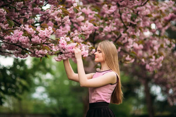 Sevimli kız pembe bluz ve siyah etek güzel çiçekli ağaçlar arka plan üzerinde fotoğrafçılar için poz veriyor. Bahar. Sakura. — Stok fotoğraf