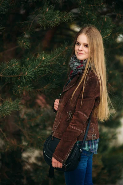 Una hermosa chica está caminando por el terraplén. Cabello rubio y chaqueta marrón. Primavera . —  Fotos de Stock