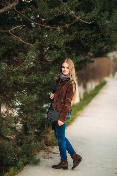 Ein schönes Mädchen läuft die Böschung entlang. blonde Haare und braune Jacke. Frühling. — Stockfoto
