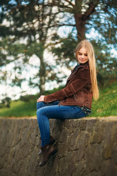 A beautiful girl is walking along the embankment. Blond hair and brown jacket. Spring. — Stock Photo, Image